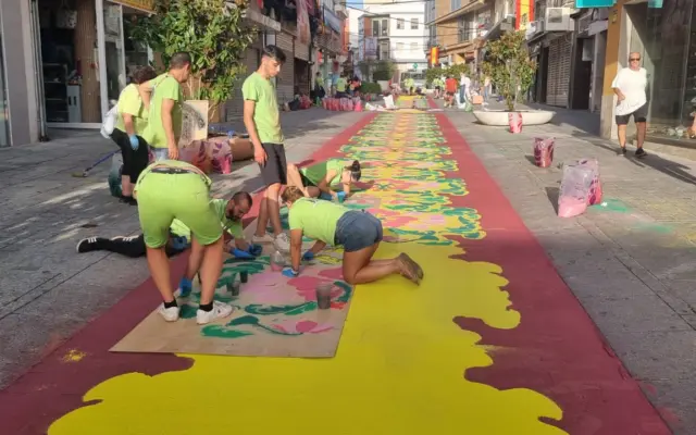 Voluntarios elaboran una alfombra de sal teñida en la calle Aduana de Puertollano para el paso de la Virgen de Gracia