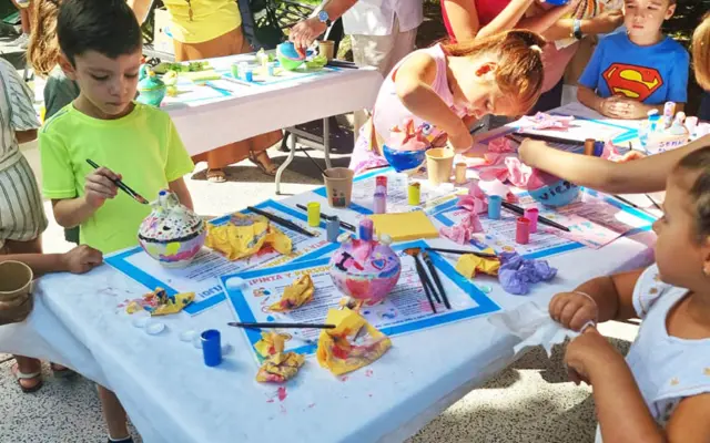 Niños y niñas pintan botijos de barro en un taller infantil durante las fiestas de Puertollano