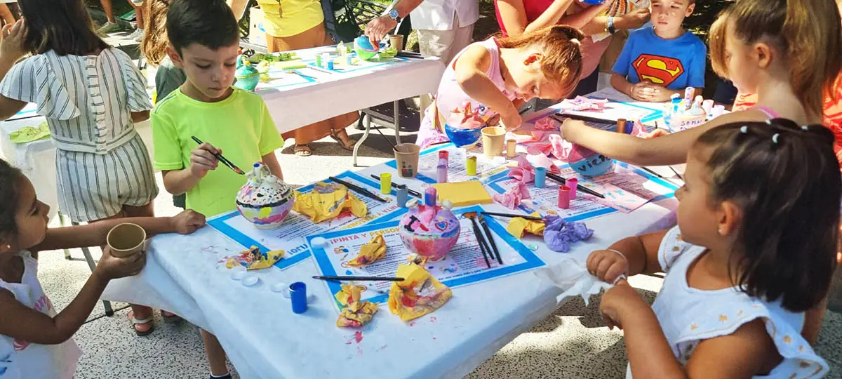 Niños y niñas pintan botijos de barro en un taller infantil durante las fiestas de Puertollano